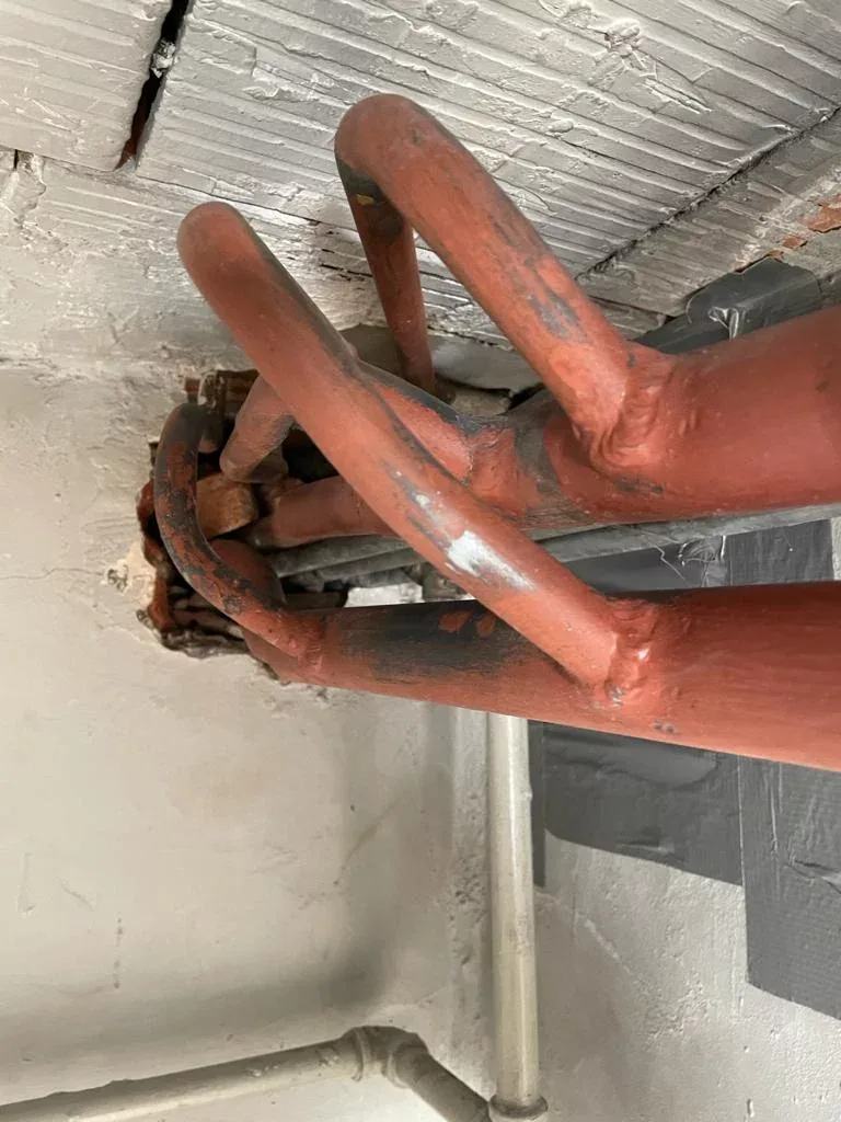 Asbesthoudende isolatie rond leidingen tegen een kelderplafond